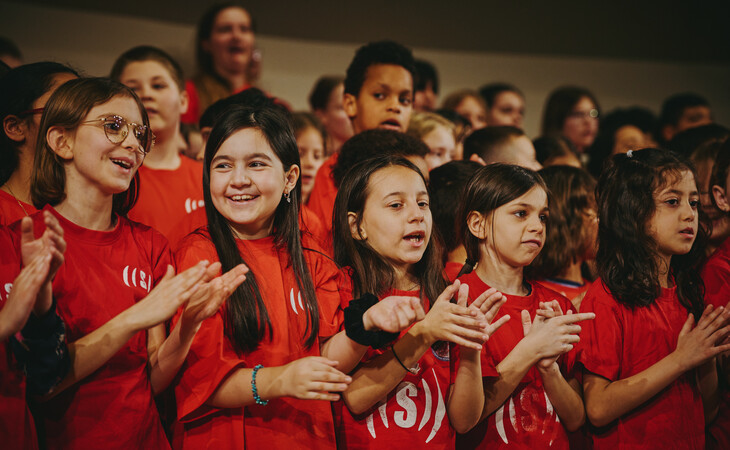 Kinderchor mit mehreren Kindern in roten T-Shirts, die gemeinsam singen und klatschen