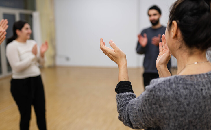 Gruppe von Menschen steht in einem Raum und klatscht, eine Person ist im Vordergrund von hinten zu sehen